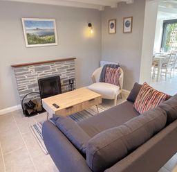 A living room with a gray sofa, armchair, coffee table, fireplace, and wall art at Kernyk in Perranuthnoe