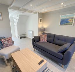 A living room with a dark sofa and light armchair with striped cushions and a wooden coffee table at Kernyk in Perranuthnoe