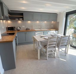 A kitchen with gray cabinets wooden countertops a dining table set for four near a sliding glass door at Kernyk in Perranuthnoe