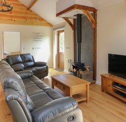 A living room with leather sofas a wooden coffee table a wood stove and a television at Ploony Hill Cabin in Bleddfa near Knighton