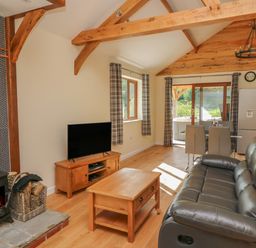 A living room with a leather couch wooden coffee table TV wood stove and dining table at Ploony Hill Cabin in Bleddfa near Knighton