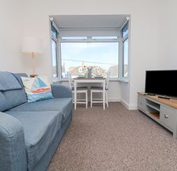 A living room with a blue sofa a floor lamp a dining table with two chairs and a television on a cabinet at The Beach Hut in St Ives