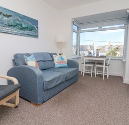A seating area with a blue sofa and armchair with a dining table and chairs by a large window at The Beach Hut in St Ives