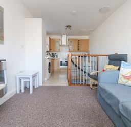 A living room with a blue sofa and chair next to a railing with a kitchen in the background at The Beach Hut in St Ives