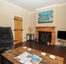 A living room with a black chair wooden door wood-burning stove television and a wooden coffee table with a magazine at Weybury Cottage Brewers Quay Harbour