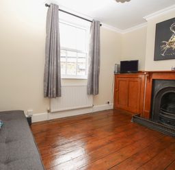 A room with wooden floor a sofa a window with curtains a fireplace and a small television at Weybury Cottage Brewers Quay Harbour
