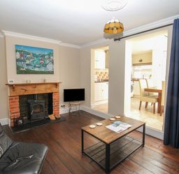 A living room with a fireplace a black leather chair a wooden coffee table and a view into a kitchen at Weybury Cottage Brewers Quay Harbour