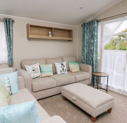 A living room with sofas cushions ottoman small round table and windows with blue curtains at Ystwyth 26 in Borth