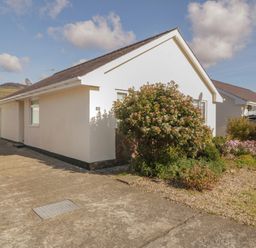 A single-story house with a concrete driveway and garden bushes at Seaside retreat in Porthmadog