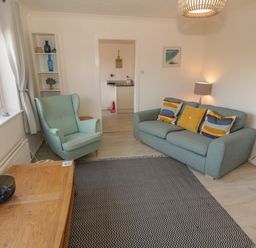 A living room with a blue sofa with cushions an armchair a wooden coffee table and a patterned rug at Seaside retreat in Porthmadog