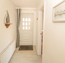A hallway with a white door at the end a striped curtain a sailboat decoration on the wall a radiator and a framed picture on the wall at Seaside retreat in Porthmadog