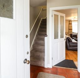 An entryway with a partially open white door showing stairs and an open doorway to a living room with leather sofas at Artro View in Llanbedr