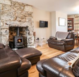 A living room with leather sofas a stone fireplace and a wall-mounted television at Artro View in Llanbedr