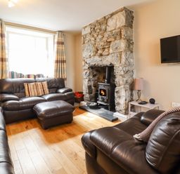 A living room with leather sofas a stone fireplace with a stove a mounted tv and a window with striped curtains at Artro View in Llanbedr