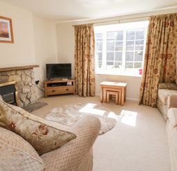 A living room with stone fireplace television wooden tables and patterned curtains at Crooked Well in Timsbury Nr Bath