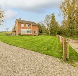 A brick house with a gravel driveway and a green lawn surrounded by trees at Orchard House in Risbury near Leominster