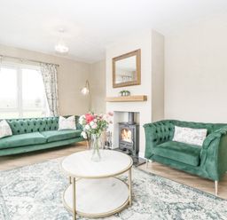 A living room with green sofas a round coffee table with flowers and a fireplace at Orchard House Risbury near Leominster