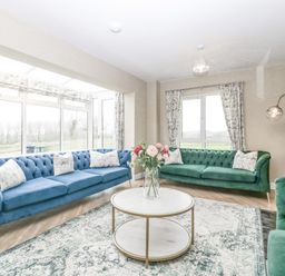 A living room with blue and green sofas a round coffee table with flowers and large windows at Orchard House in Risbury near Leominster