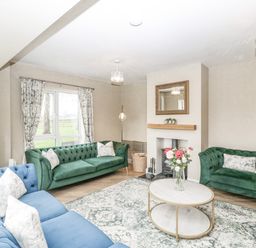 A living room with green and blue sofas a round coffee table and a fireplace at Orchard House in Risbury near Leominster