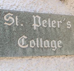 A stone plaque with the text St Peters Cottage mounted on a textured wall at St Peters Cottage in Milnthorpe