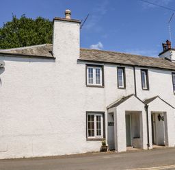 A white two story cottage with multiple windows and two porch entrances at St Peters Cottage in Milnthorpe