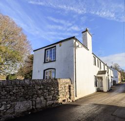 A white house with a stone wall in front and a road beside it at St Peters Cottage in Milnthorpe