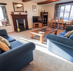 A living room with blue sofas a wooden coffee table fireplace television dining table and chairs at St Peters Cottage in Milnthorpe