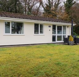 A small cream-colored cottage with three windows and a glass door with outdoor table and chairs on the lawn at Blue Sky Cottage in Rosecraddoc Lodge near Liskeard