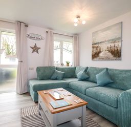 A living room with a blue-green corner sofa a wooden coffee table and a beach painting at Blue Sky Cottage Rosecraddoc Lodge near Liskeard