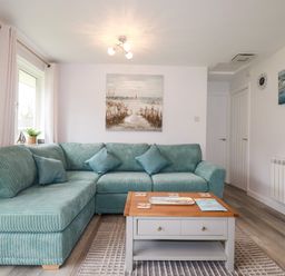 A living room with a teal sectional sofa a wooden coffee table and coastal paintings at Blue Sky Cottage Rosecraddoc Lodge near Liskeard