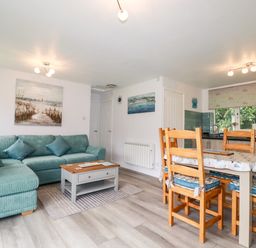 A living room with a green sectional sofa a wooden coffee table a dining table with chairs and a kitchen area at Blue Sky Cottage Rosecraddoc Lodge near Liskeard