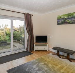 A room with a sliding glass door with curtains a small television on a stand two stools and a rug on a wooden floor at The Annex in Drybrook