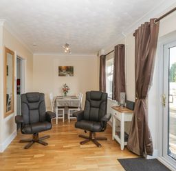 A dining area with a table and chairs two black armchairs wooden flooring and a glass door with curtains at The Annex in Drybrook