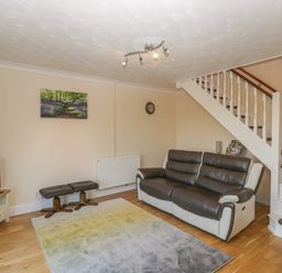 A living room with a sofa two stools a carpet television under stairs and a wall clock at The Annex in Drybrook