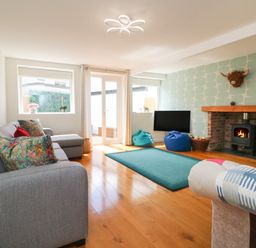 A living room with a gray sectional sofa colorful pillows a fireplace a mounted television bean bags and wooden flooring at The Old Coach House in Braunton