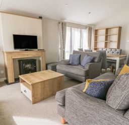A living room with two gray sofas a wooden coffee table a TV on a wooden mantel and a dining table with chairs and a wooden shelf at Daisy Lodge in Cayton Bay near Cayton