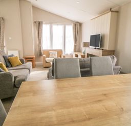 A living room with a wooden table gray chairs a gray sofa an armchair a television and curtains at Daisy Lodge in Cayton Bay near Cayton
