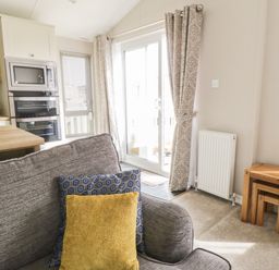 A living area with a gray sofa with cushions and wooden nesting tables near a radiator and sliding glass door at Daisy Lodge in Cayton Bay near Cayton