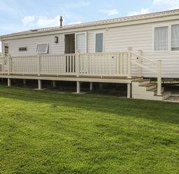 A white mobile home with a wooden deck and steps on a grassy lawn at Daisy Lodge in Cayton Bay near Cayton