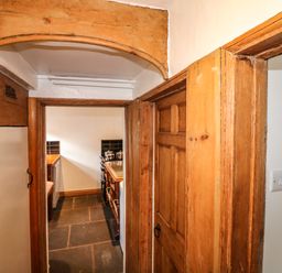 A hallway with wooden door frames leading to a kitchen with a stove and countertop at Hops Cottage in Doveridge