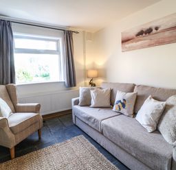 A living room with a grey sofa with pillows an armchair near a window and a lamp at Hops Cottage in Doveridge