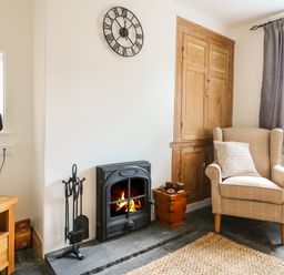 A living room with a fireplace an armchair a wooden cabinet and a television at Hops Cottage in Doveridge