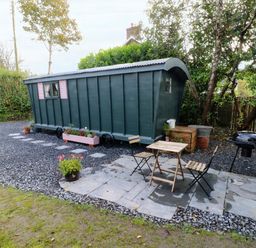 A small wooden cabin with pink shutters a small table and two chairs a barbecue grill and potted plants in a garden at Hazel Nook in Narberth