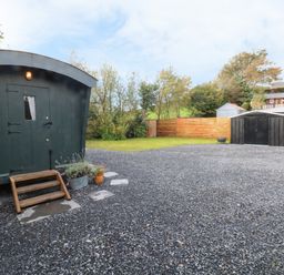 A gravel yard with a dark green shed a black metal storage shed potted plants and wooden fence at Hazel Nook in Narberth
