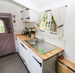 A kitchen with a wooden countertop a stainless steel sink and a purple door with curtains at Hazel Nook in Narberth