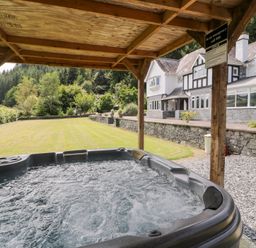 A hot tub under a wooden shelter in the garden at Pengwern in Llanrwst