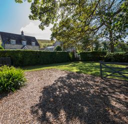 A garden with gravel driveway and green lawn with trees and a house in the background at St Marys Chapel in West Lulworth
