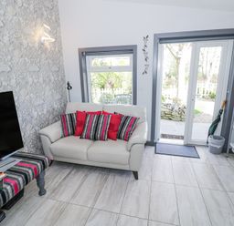 A sitting area with a white sofa with cushions a television and patio doors leading outside at The Garden House in Upper Quinton near Lower Quinton
