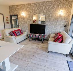 A living room with two white sofas with red and striped pillows a TV on a striped table and a white table with flowers at The Garden House in Upper Quinton near Lower Quinton