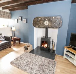 A living room with a wood stove fireplace a chair a side table and a television at Afallon in Penmachno